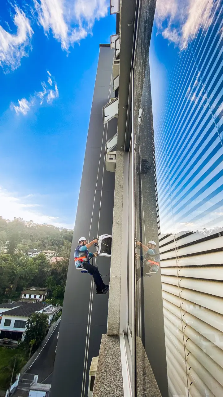 Técnico instalando ar-condicionado por rapel em fachada de prédio