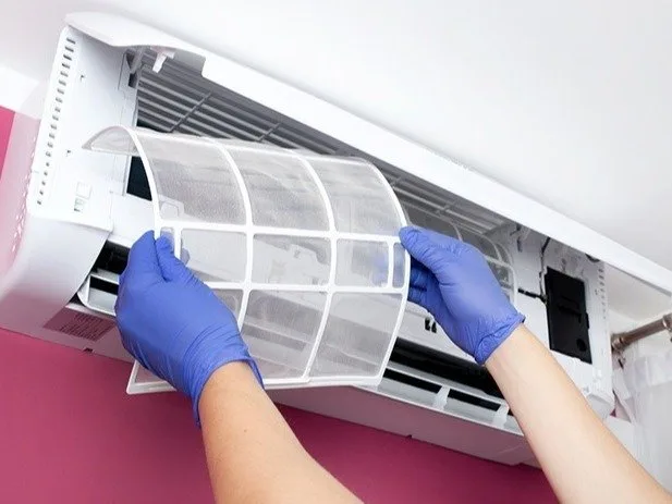 Profissional com luvas removendo o filtro de um ar-condicionado split para higienização
